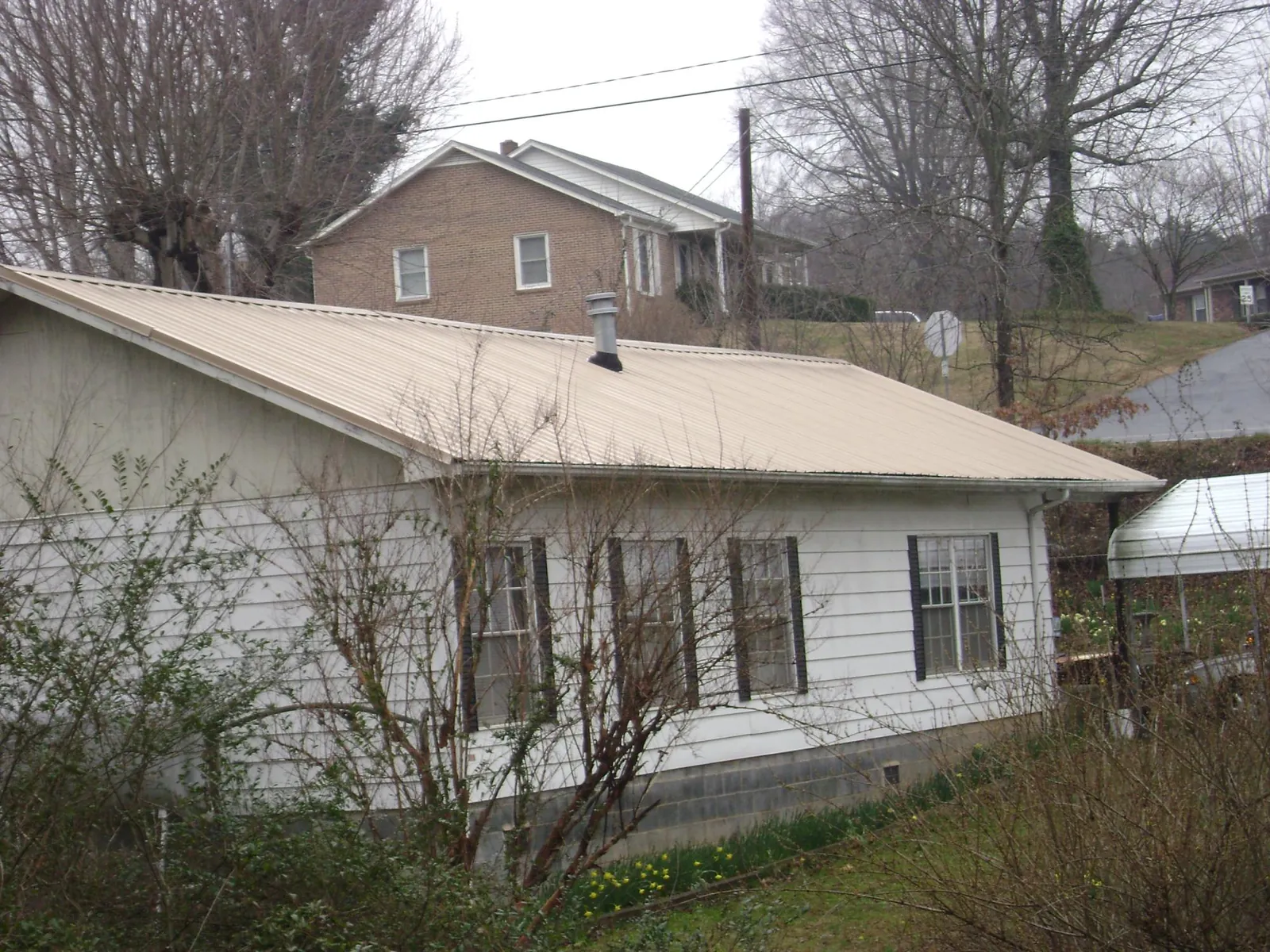 Tan metal roof on a white sided house set into a hillside — Commercial Roofing by Roofing Brothers in Redondo Beach